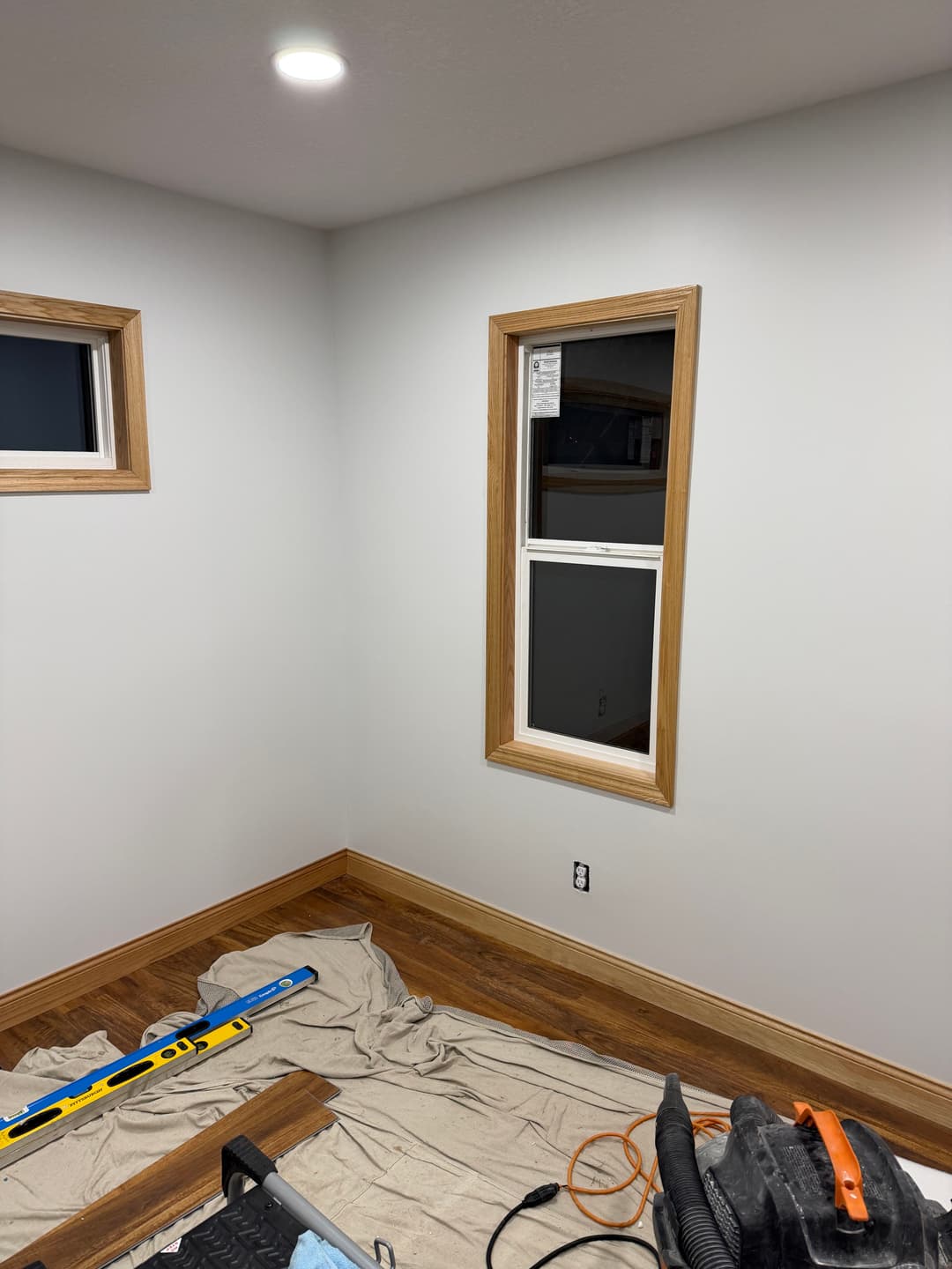 Interior view of newly painted room with window and wooden trim, tools on floor.