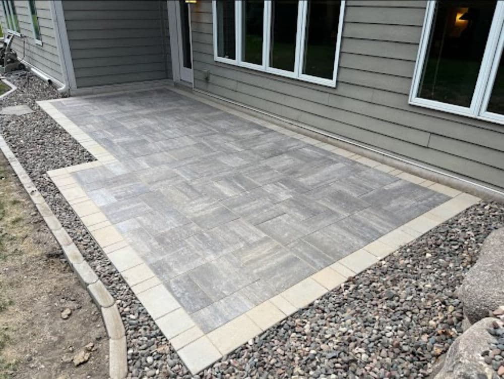 Newly installed gray paver patio beside a house with gravel landscaping.
