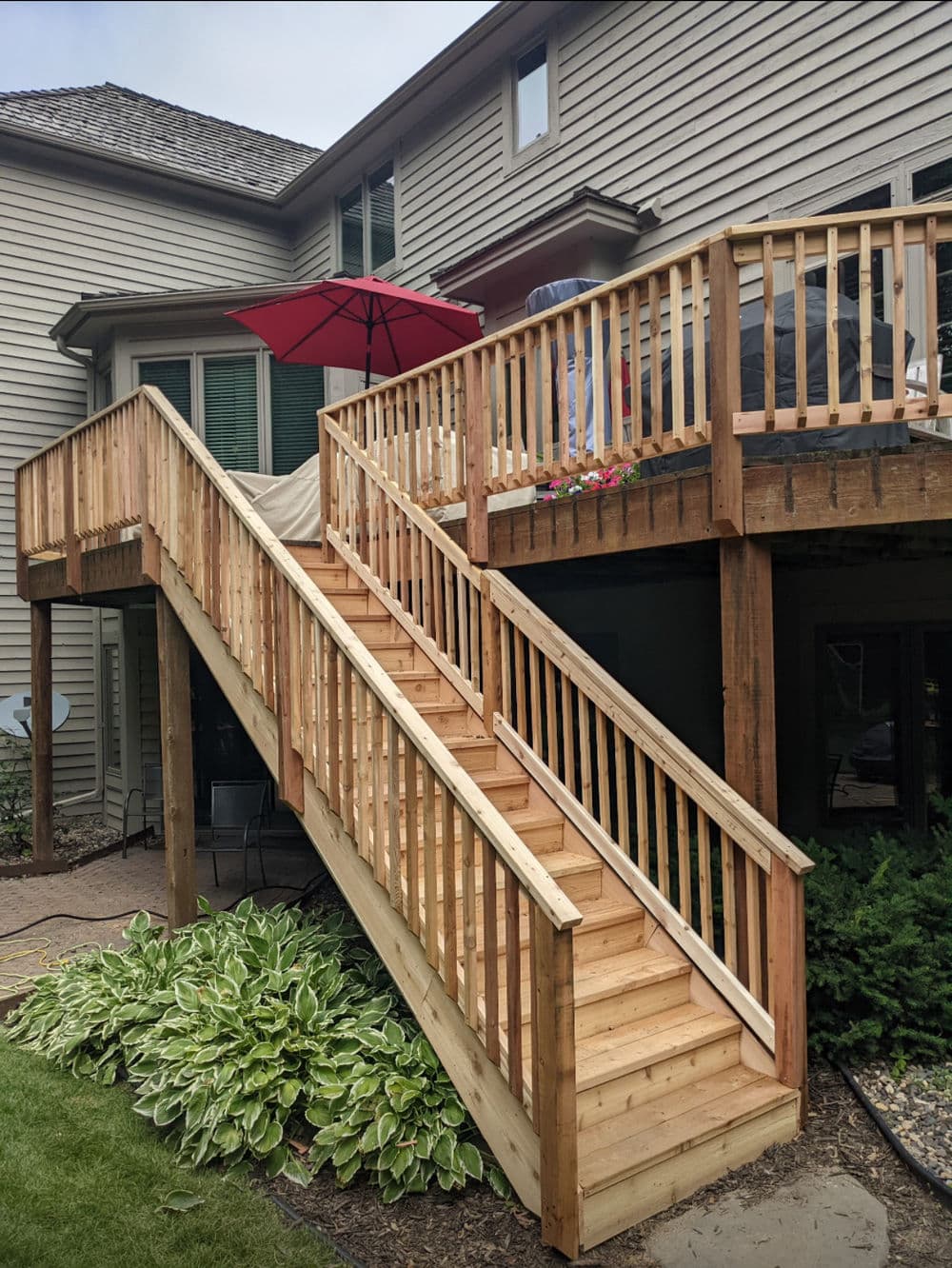 Wooden deck with stairs and umbrella, featuring a well-maintained garden area.