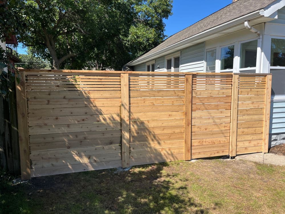 Modern wooden privacy fence with horizontal slats, situated beside a house and garden.