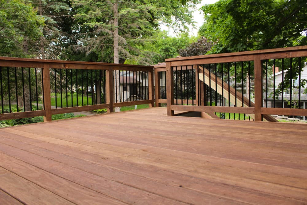 Spacious wooden deck with black railings surrounded by lush greenery. Ideal outdoor space.