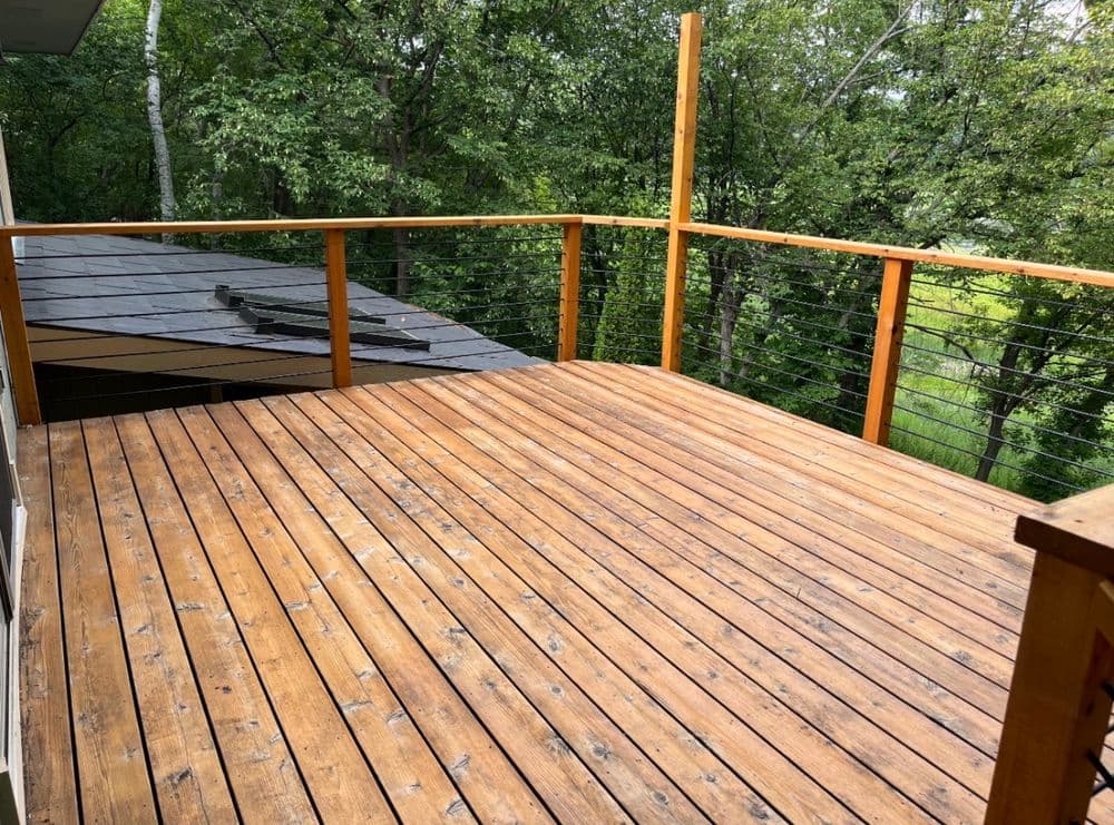 Spacious wooden deck with railing, surrounded by lush greenery and trees.